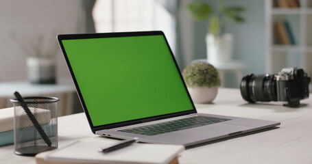 Modern laptop with mock up chroma key green screen on table of living room, desk set up for work at...