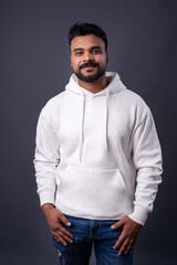 Smiling positive emotions man with dark hair, mustache beard in gray (grey) background wearing white hoodie empty print copy space. Man looking at camera and smiling. White casual sports clothes 