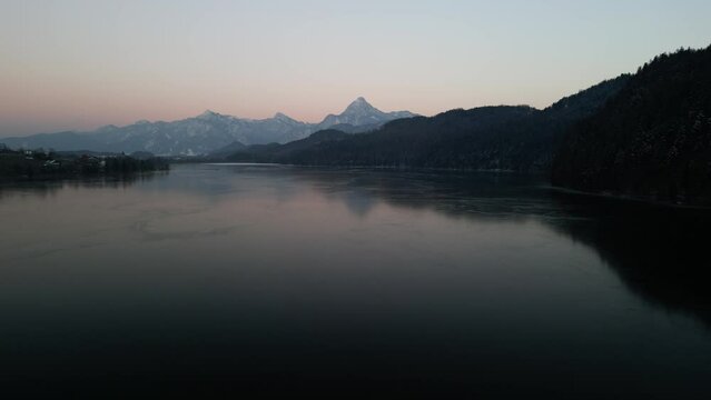 the Wei&szlig;ensee in the south of Bavaria with mountains covered with snow in the background filmed during the sunset with a drone and the lake in the foreground