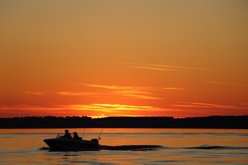 Silhouette of two fisherman on the boat. Beautiful sunset on the background.
