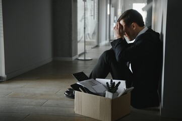 Sad fired businessman sitting outside meeting room after being dismissed.