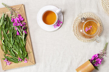 Fireweed tea in white cups and transparent glass teapot, herbal hot tea from green leaves of ivan chai on textile tablecloth. Top view healthy drink and wild flowering willow-herb, tea time