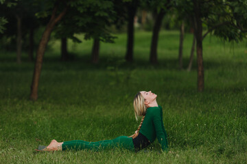 Fototapeta premium Young woman doing cobra pose on yoga mat in the park on a body summer evening.