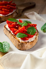 Front vertical view of three pieces of bruschetta on a plate with cherry tomatoes, cream cheese and mint leaves on a wooden table