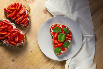 Top view of bruschetta on a plate with cherry tomatoes, cream cheese and mint leaves on a wooden table