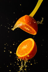 Vertical view of two halves of orange suspondend with splashes of orange juice with black background
