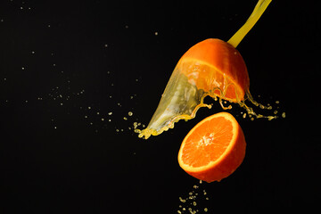 Two halves of orange suspondend with splashes of orange juice with black background