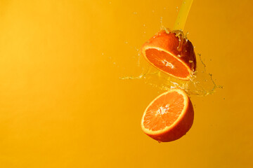 Two halves of orange suspondend with splashes of orange juice with yellow background