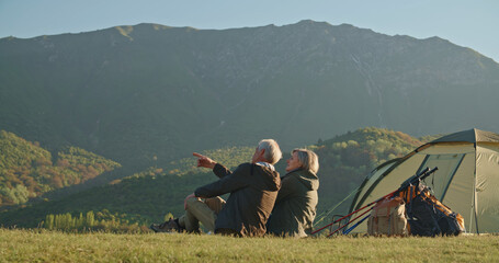 Happy senior couple sitting in summer at the top of the mountain, looking into the distance, Joyful nice elderly couple smiling while being in a great mood