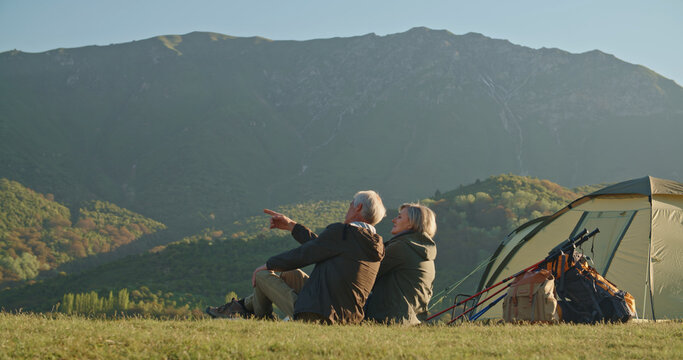 Happy Senior Couple Sitting In Summer At The Top Of The Mountain, Looking Into The Distance, Joyful Nice Elderly Couple Smiling While Being In A Great Mood