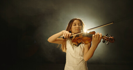 Female violin player performing sheet music on stage. Experienced asian violin player having solo concert, spotted by light on black background 