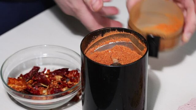 A man grinds dried red peppers in a coffee grinder. Demonstrates the degree of grinding in a coffee grinder. Grinding hot pepper. Close-up.