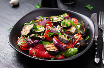 Grilled vegetables eggplant, bell pepper, zucchini, red onion, tomato with garlic on a black plate.