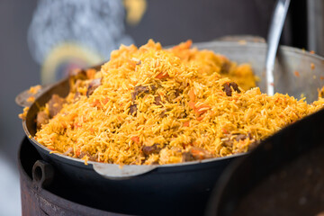 Rice with meat, carrots in big cauldron, traditional dish of pilaf, national cuisine, street food in outdoor on food market