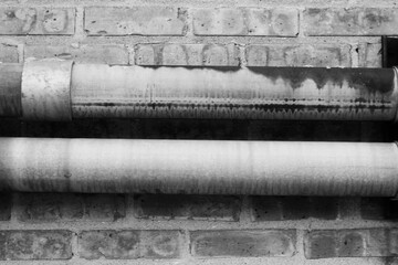 Rusty metal pipe on a brick wall in black and white.