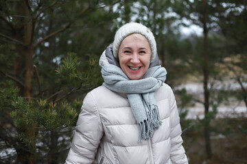 Portrait of happy beautiful elderly senior retired woman in age is playing, having fun with snow outdoors in forest or park at winter cold day, smiling, enjoy weather