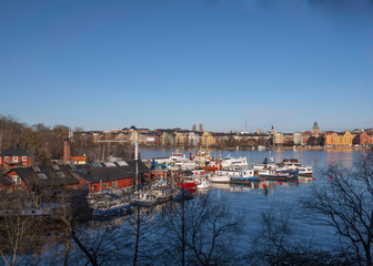Fototapeta premium View from the district Södermalm over the bay Riddarfjärden with the Town City Hall and down town, wharf with fishing, tug and steam commuting boats, a sunny winter day in Stockholm