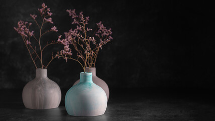 Three plaster vases of dried flowers on а black background, front view copy space, selective focus, low key. Home decor.