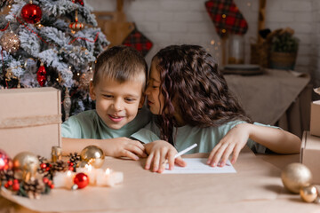 boy and girl write a letter with Christmas wishes to Santa Claus, sitting at a wooden kitchen table