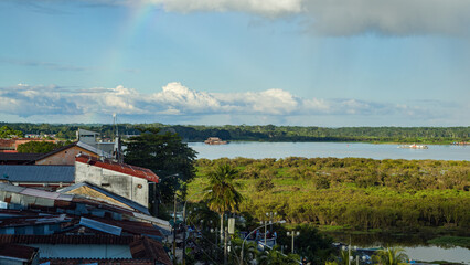 Fototapeta na wymiar Rainbow over buildings and The Amazon Rainforest and River. Iquitos, Peru