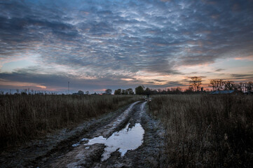 The field road between the villages is covered with puddles that reflect the colors of the dawn sun.