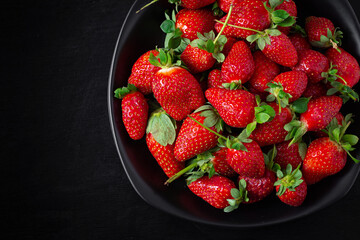 Strawberries in a black plate on dark background. Top view, above