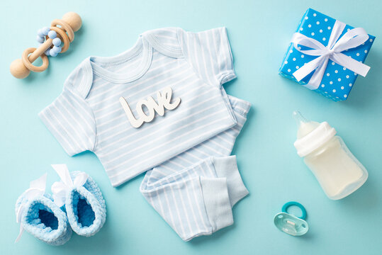 Baby boy concept. Top view photo of blue shirt pants inscription love knitted booties giftbox milk bottle pacifier and wooden rattle on isolated pastel blue background