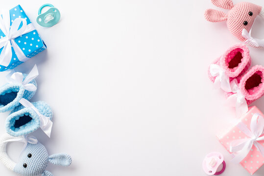 Gender reveal party concept. Top view photo of pink and blue knitted booties gift boxes bunny rattle toys and soothers on isolated white background with copyspace
