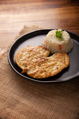 Homemade grilled chicken breast, (butterflyed) flattened and seasoned. Accompanied by white rice served in a dark plate on a rustic wooden table.