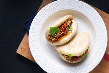 Food concept Homemade organic Pulled Beef Bao Buns or Gua Bao in white ceramic plate on black...