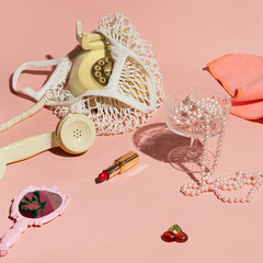 Rotary dial phone in a mesh bag, lipstick, retro style hand mirror, pearls, coupe champagne glass,...