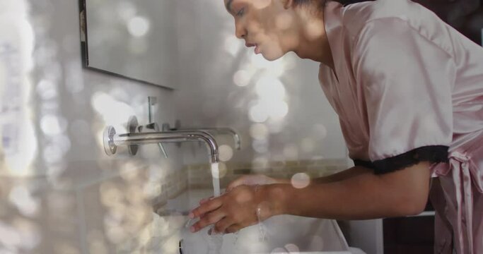 Animation of glowing lights over biracial woman washing face