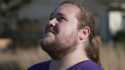 Fototapeta premium Young man close up face looking at sky with HOPE and FAITH. One contemplative chubby guy looks up. Tracking shot