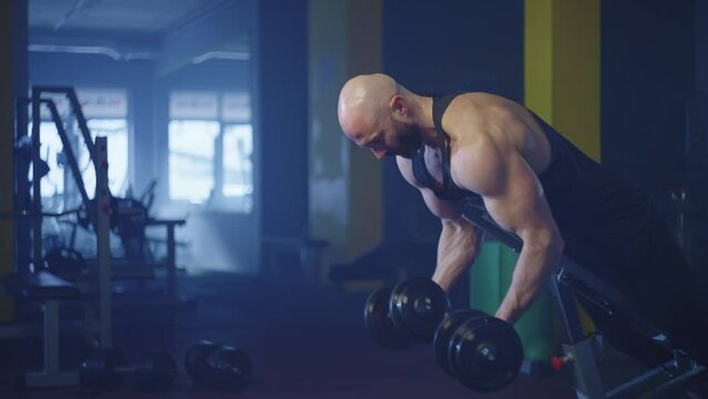 A healthy and sports lifestyle. Athletic man working out with dumbbells in the gym. Bodybuilder swings his arms while lifting weights. Workout and fitness in the hall.
