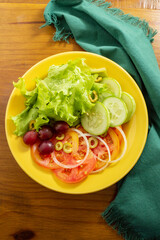 Um prato amarelo com salada de legumes, sobre um guardanapo verde, em uma mesa de madeira.