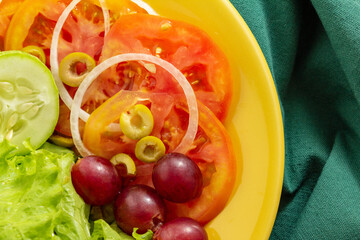 Um prato amarelo com salada de legumes, sobre um guardanapo verde. Comida vegana.