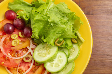 Detalhe de um prato amarelo com salada de legumes, sobre uma mesa de madeira.