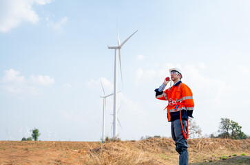 Engineer or technician worker use walkie talkie to communicate his co-worker and stand in front of windmill or wind turbine in concept of work with green ecology support power.
