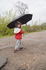 A small child stands under an umbrella. the child hid behind an umbrella