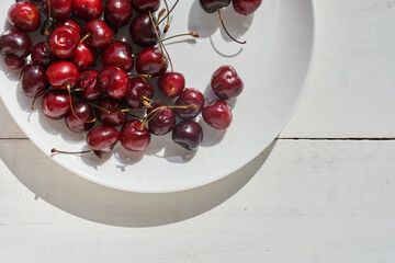 Close-up of a plate of ripe cherries in a white plate on a white wooden background. With space to copy. Top view of a plate of cherries. High quality photo