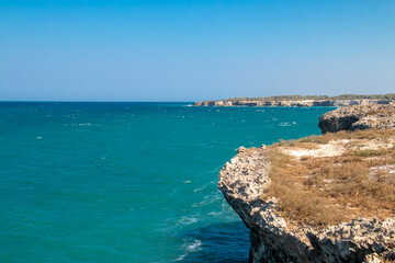 Acantilados de Roca Vecchia en Lecce, Italia. Olas de un mar Adriático azul turquesa rompiendo contra los acantilados calizos en un soleado día de verano.