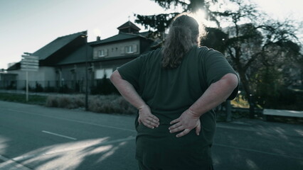 Dramatic moment of person suffering from back pain. An overweight man having physical injury outside