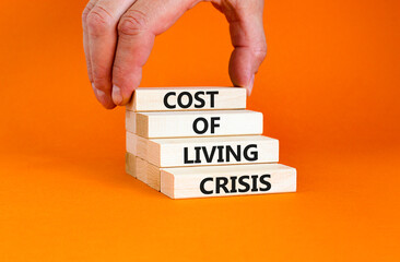 Cost of living crisis symbol. Concept words Cost of living crisis on wooden blocks. Beautiful orange table orange background. Businessman hand. Business cost of living crisis concept. Copy space.