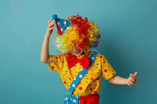 Funny kid clown against blue background. Happy child playing with festive decor. 1 April Fool's day concept