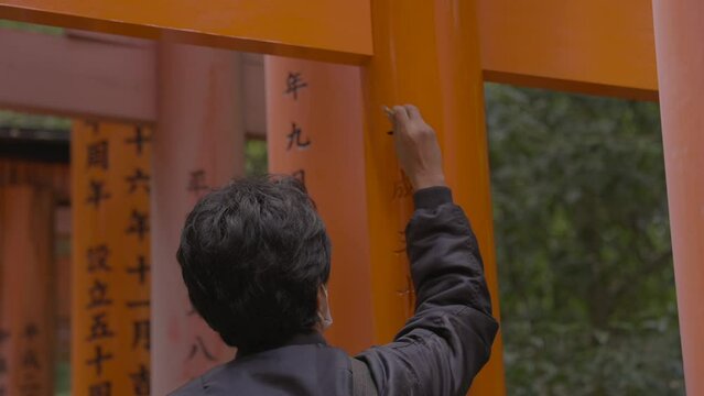 This video shows a rear view of a man repainting calligraphy on red Japanese temple torii gates.