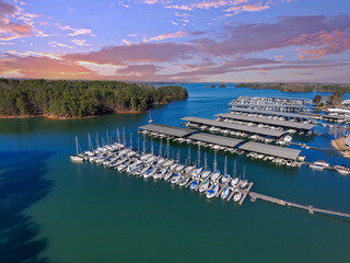 aerial shot of the boats and yachts docked in the marina on the waters of Lake Lanier surrounded by lush green trees with powerful clouds at sunset in Buford Georgia USA - obrazy, fototapety, plakaty