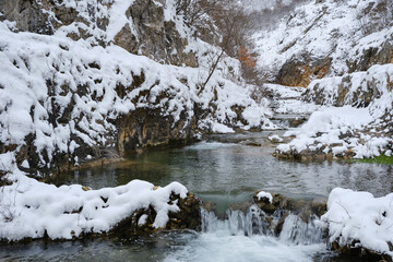 Clean, beautiful mountain creek flowing through rocky canyon covered by snow - 572012494