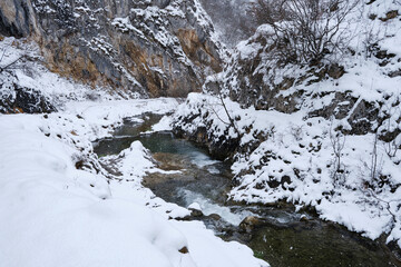 Clean, beautiful mountain creek flowing through rocky canyon on a snowy day - 572012498
