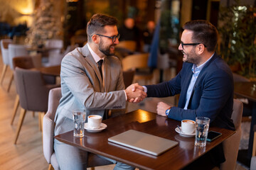 Two smiling confident male business partners at business meeting in restaurant shaking hands as sign they have reached an agreement, finishing up a meeting or setting goals, sharing productive ideas.