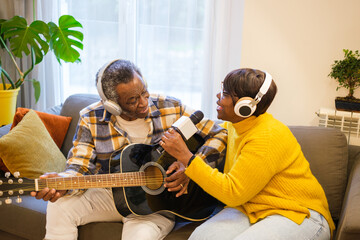 Senior couple playing the guitar and singing together in their living room enjoying their free time. Concept: retirement, music, entertainment